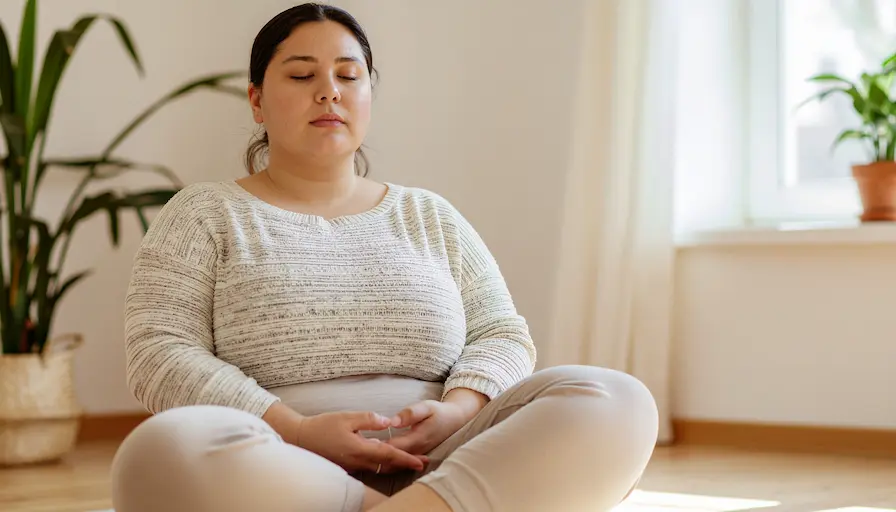Mujer latina meditando en un interior luminoso, ilustrando La Triple Aceptación como una forma de abrirse a la experiencia del momento.